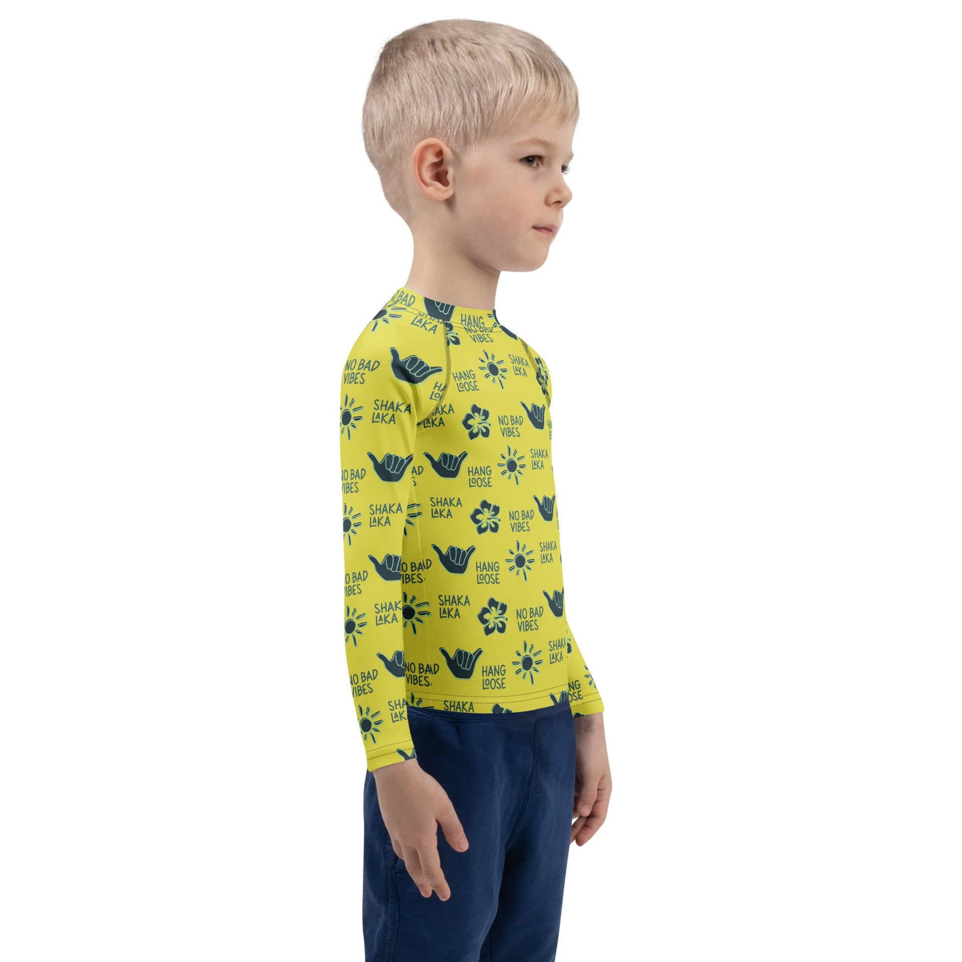 Side view of a boy wearing a yellow rash guard with navy designs of the  sun, hibiscus flowers, hang loose hand sign, and the words hang loose, no bad vibes, and shaka laka.