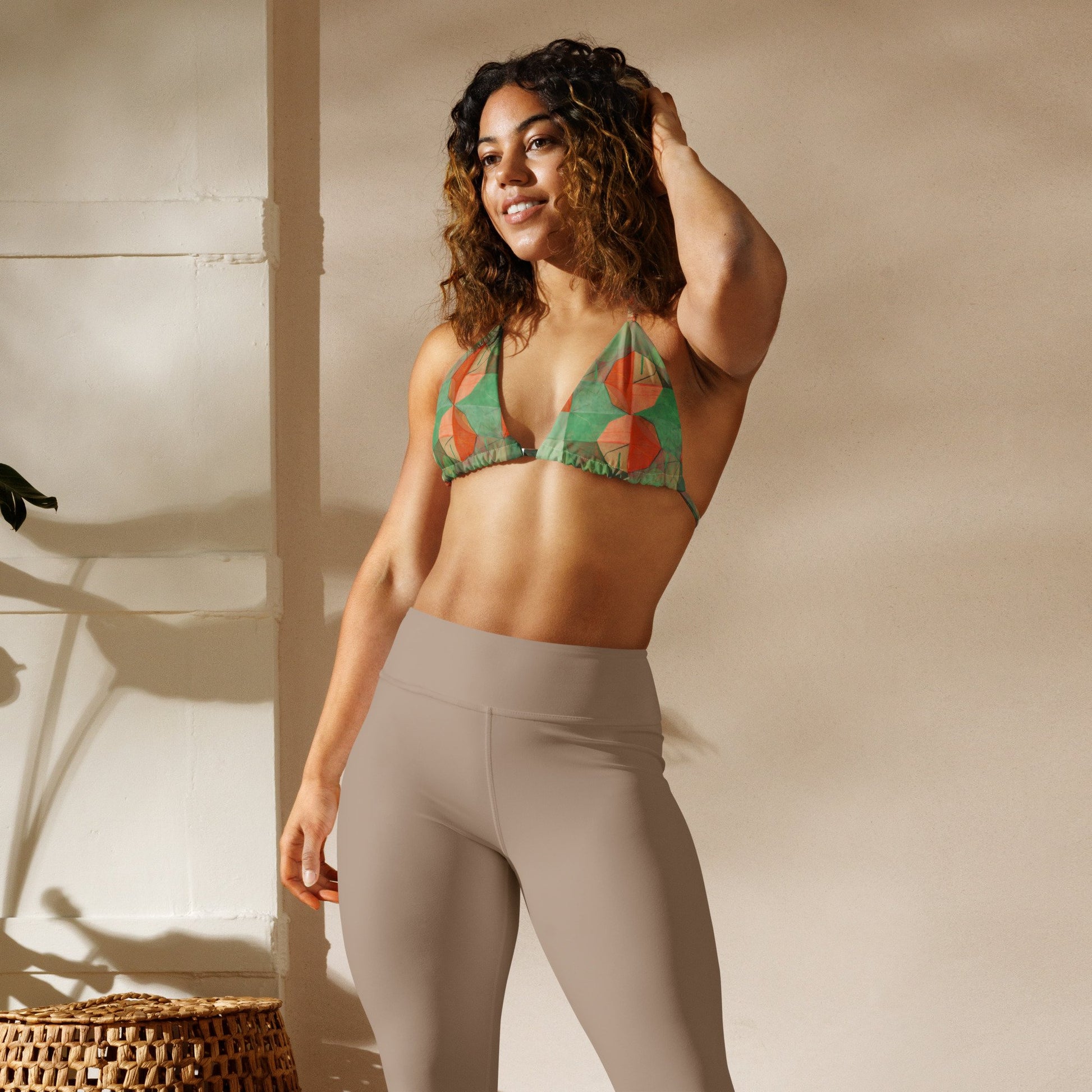 Woman wearing light and dark green colored print bikini top with orange flowers and light mocha exercise bottoms.