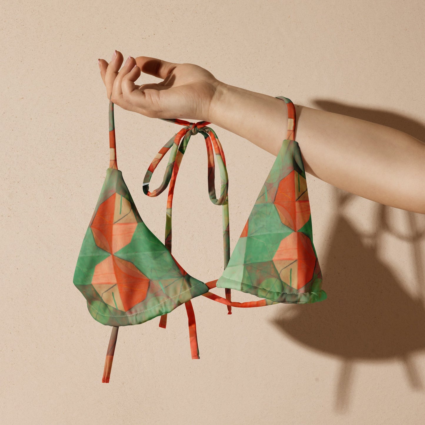 Hand holding up green and orange geometric print bikini top.