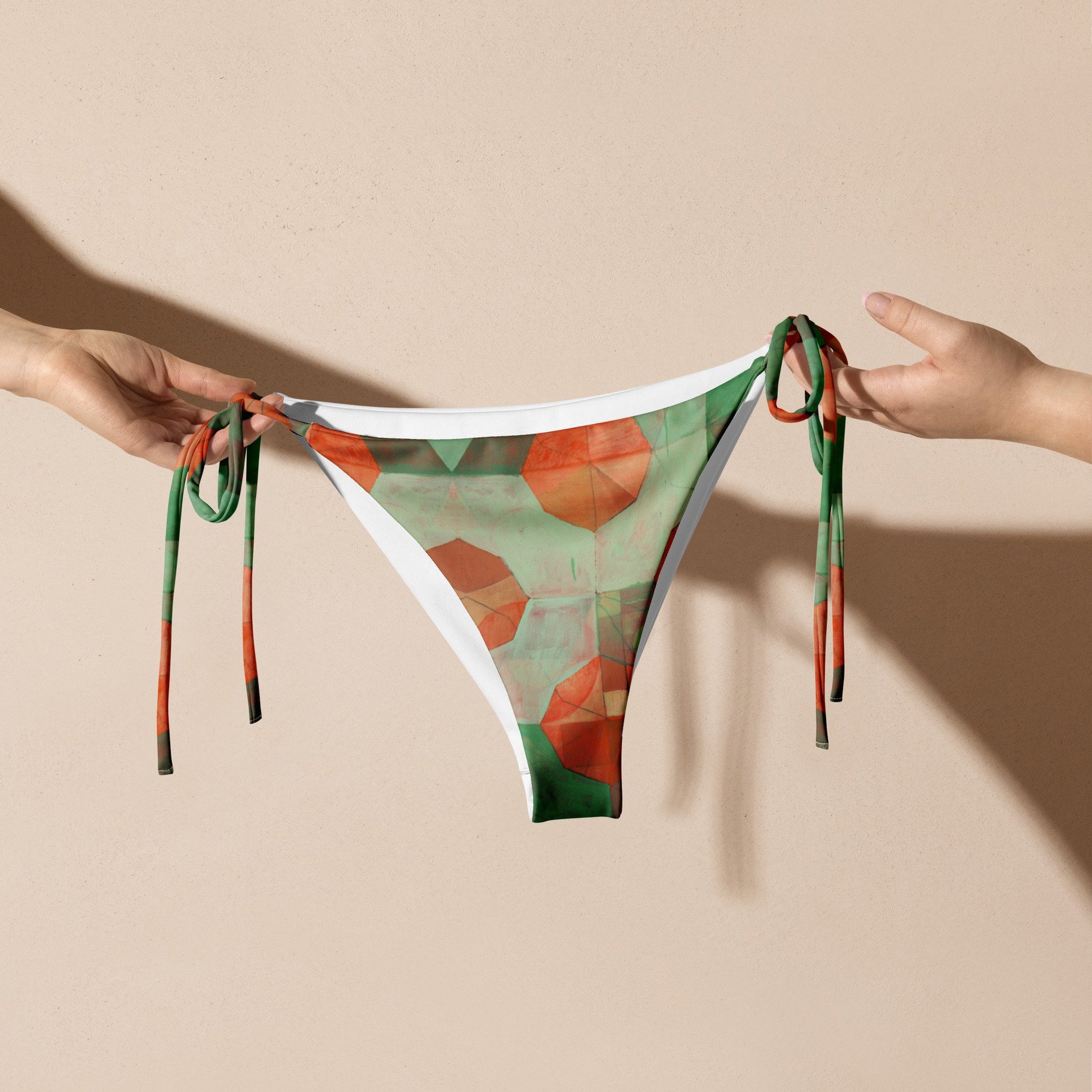 Two hands holding light and dark green with orange flowers print bikini bottoms.