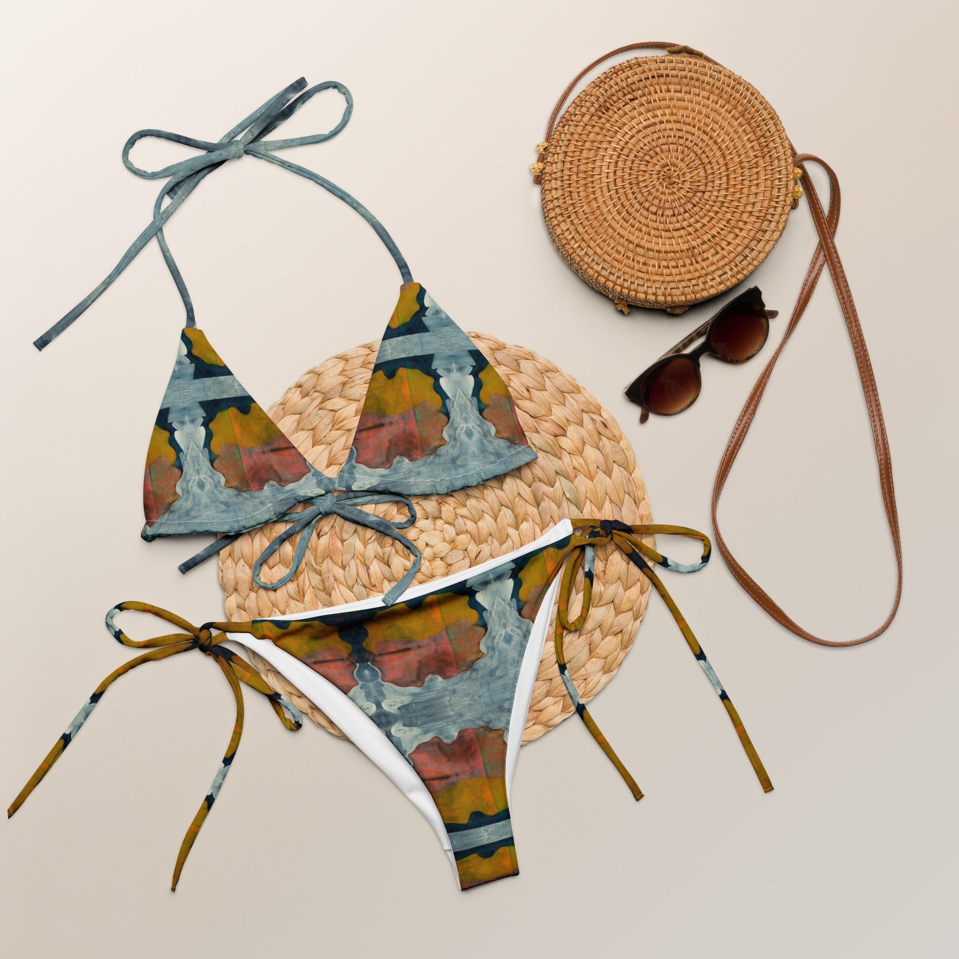 Multi colored print bikini on straw mat, next to straw purse and sunglasses.