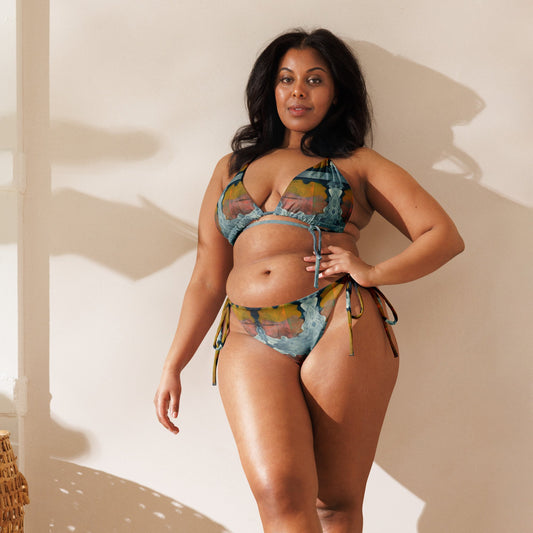 Woman leaning against shadowy wall, wearing multi colored print bikini.