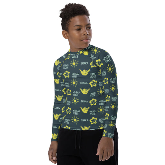 Front view of boy with dark blue rash guard with yellow designs of the sun, hibiscus flowers, hang loose hand sign, and the words hang loose, no bad vibes, and shaka.