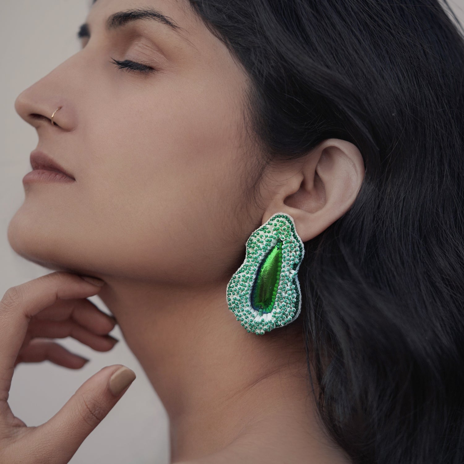Front left view of woman wearing Pennata beaded green glass earrings with iridescent centers.