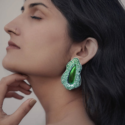 Front left view of woman wearing Pennata beaded green glass earrings with iridescent centers.