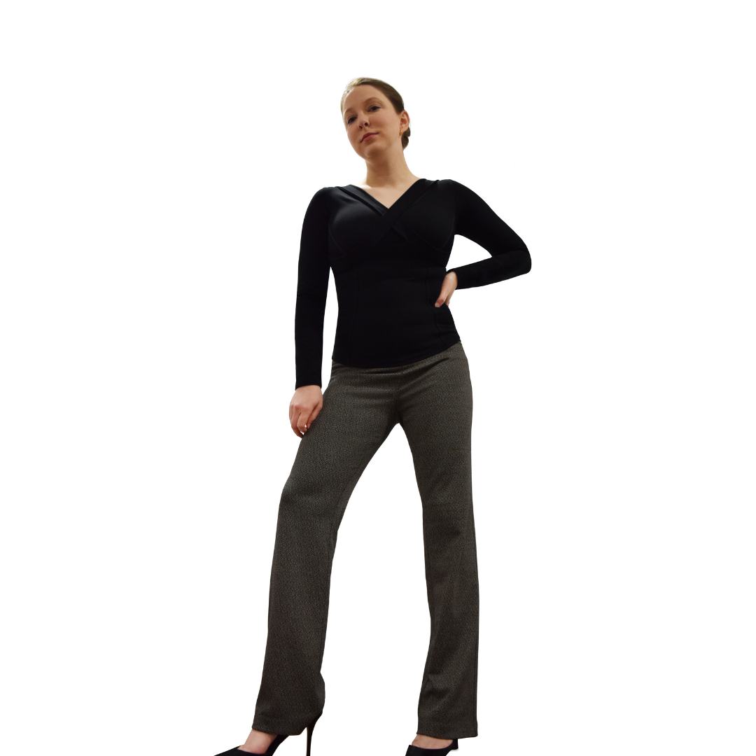 Woman wearing black long sleeve v-neck top and grey pants, right leg forward, right arm at side and left hand at waist.