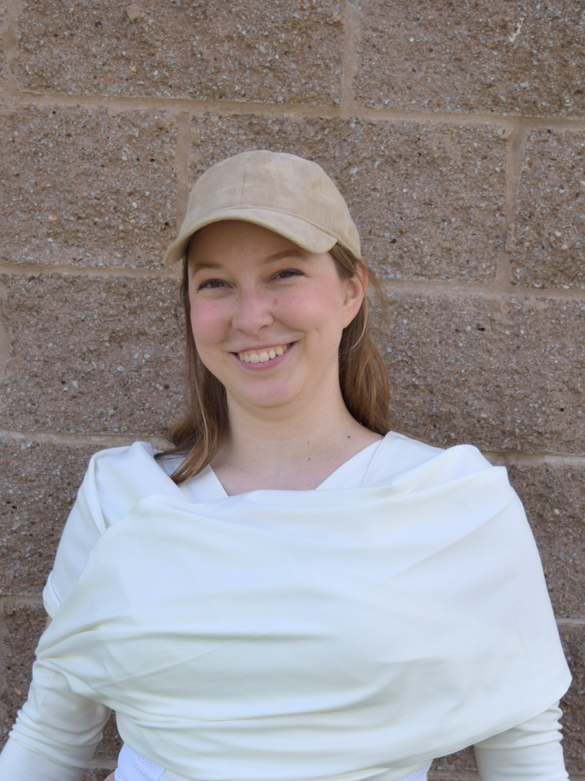 Woman with tan hat wearing a white wrap over a white shirt.