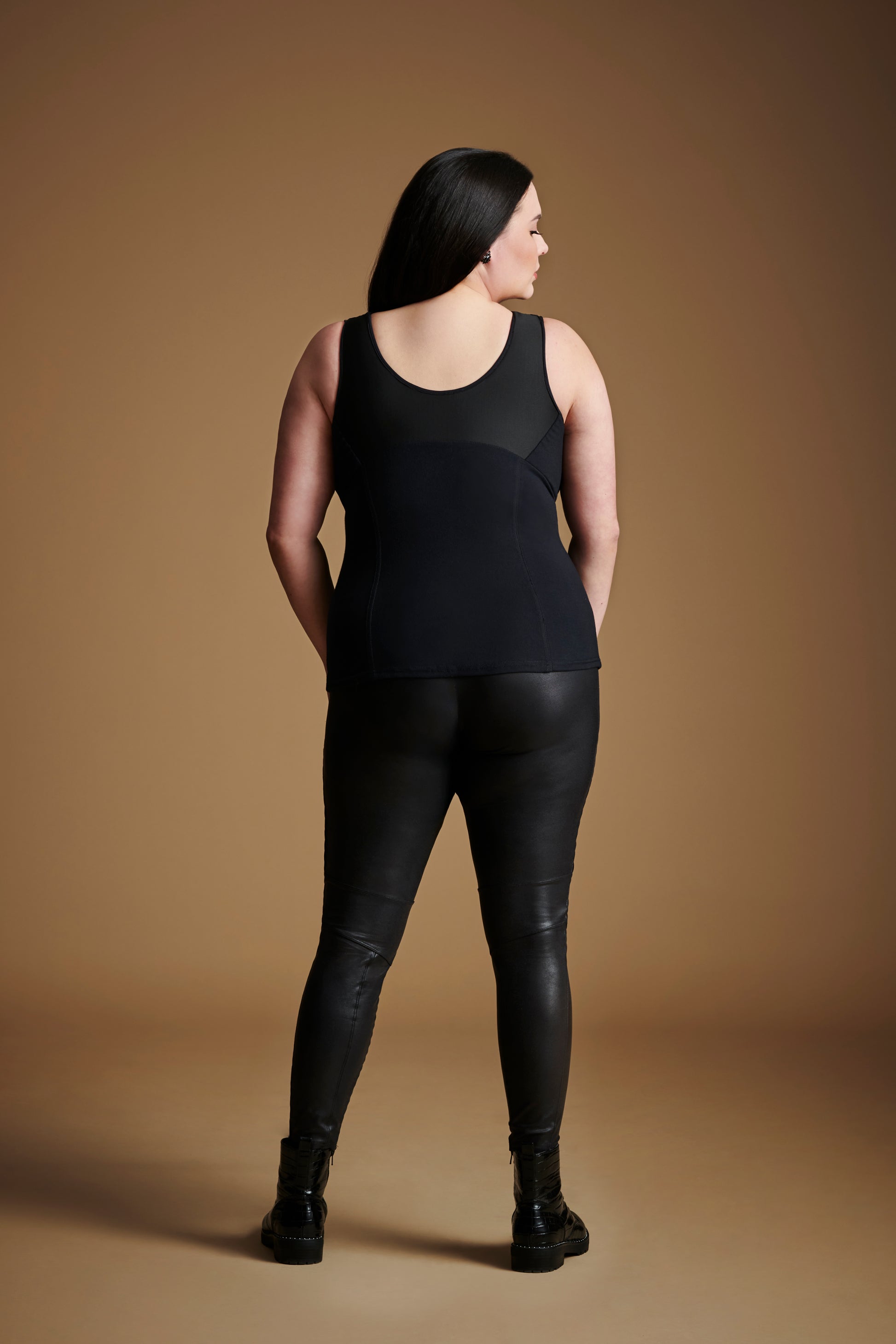 Back view of woman looking over right shoulder wearing black sleeveless v neck top.