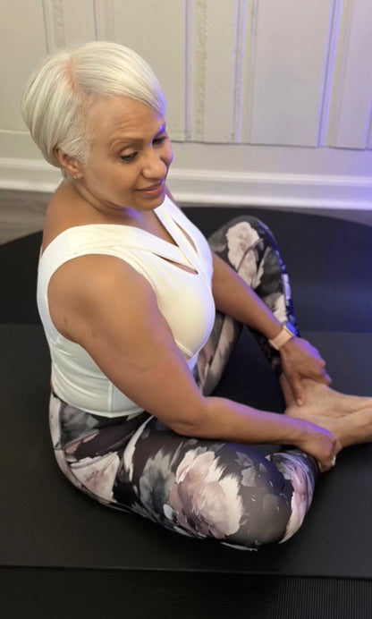 Woman in yoga pose, wearing white waist length crop top and floral exercise pants.