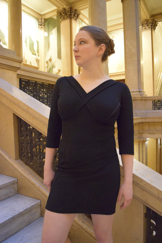 Woman on stairs looking to the right, wearing a black dress.