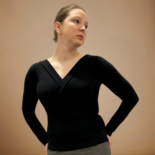 Woman wearing black V-neck long sleeve top, hands at waist.