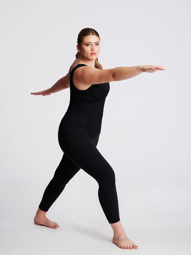 Woman standing in yoga pose, wearing black sleeveless v neck top and black pants.
