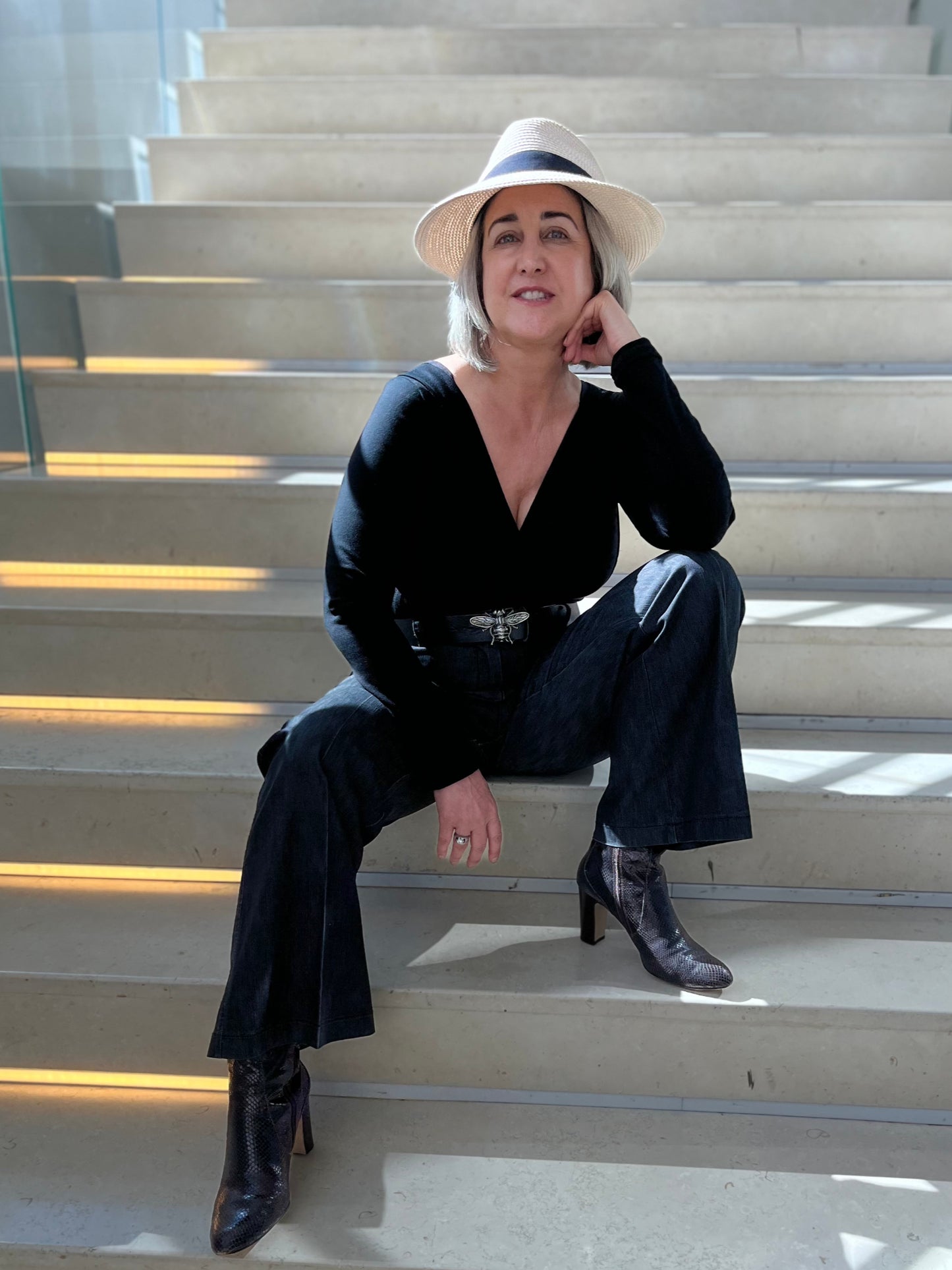 Woman sitting on steps, wearing black long sleeve v-neck top, black pants and black boots.