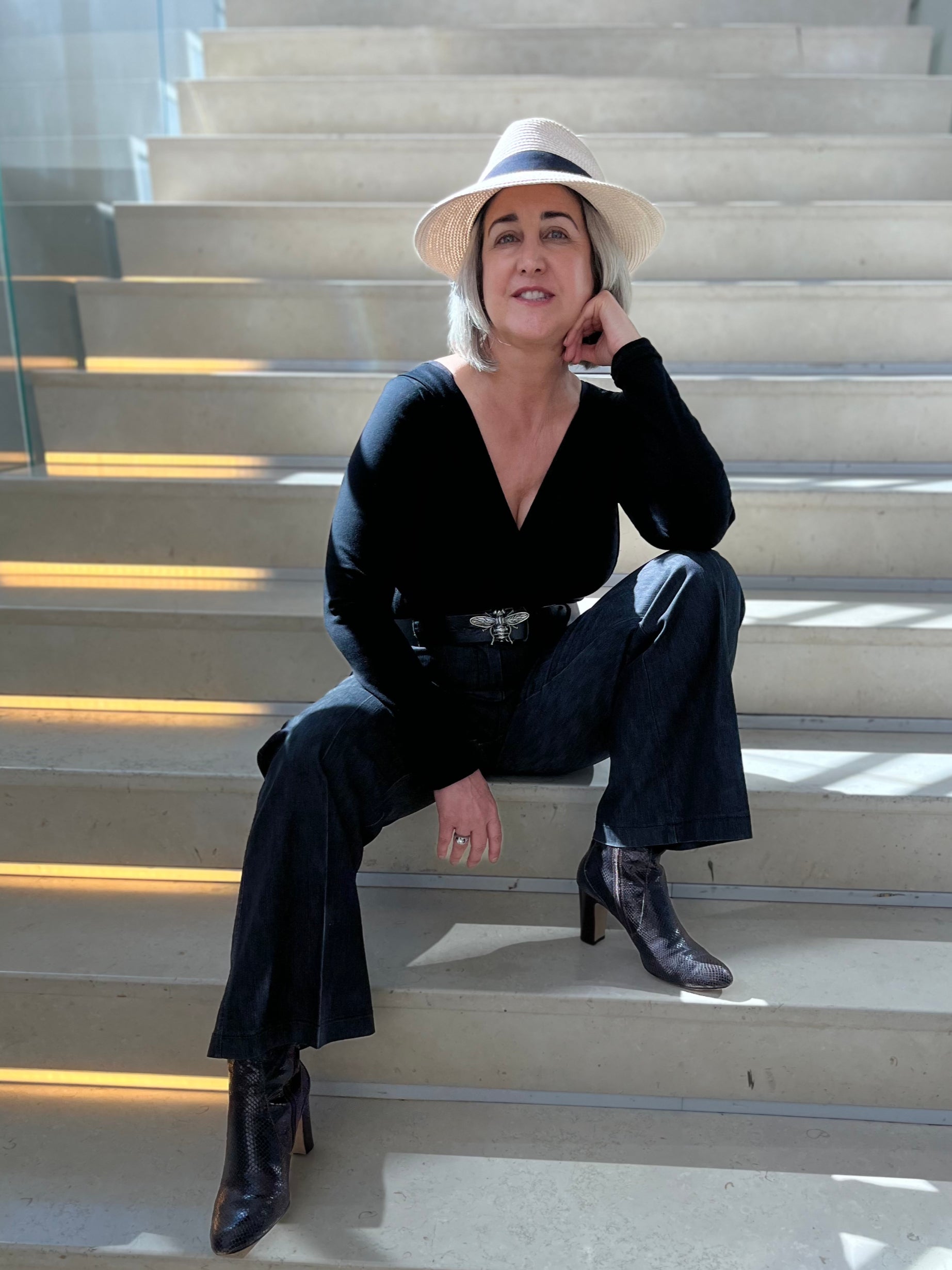 Woman sitting on steps, wearing black long sleeve v-neck top, black pants and black boots.