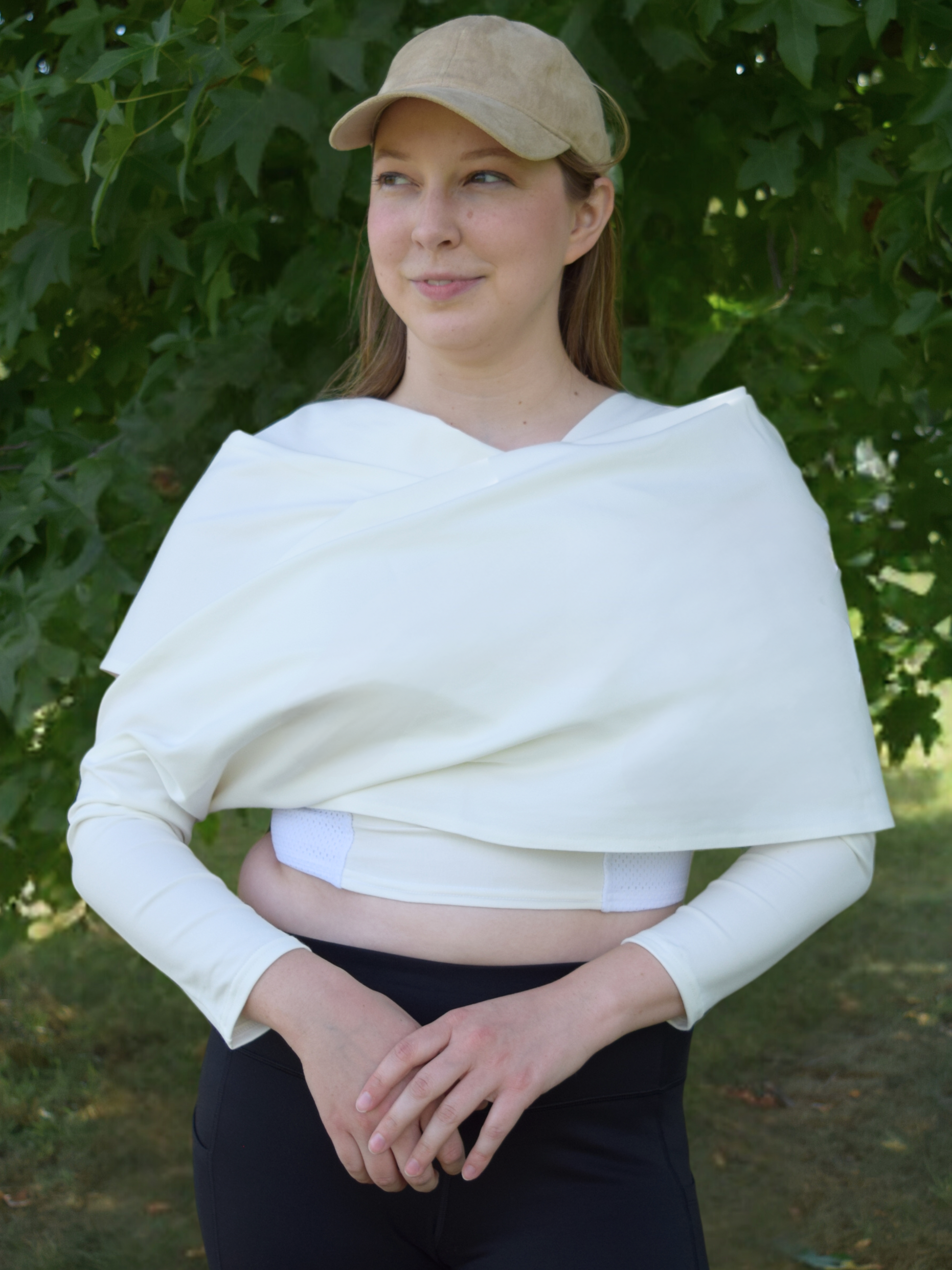 Woman wearing a tan hat and white wrap with a white crop top shirt, hands together at hips