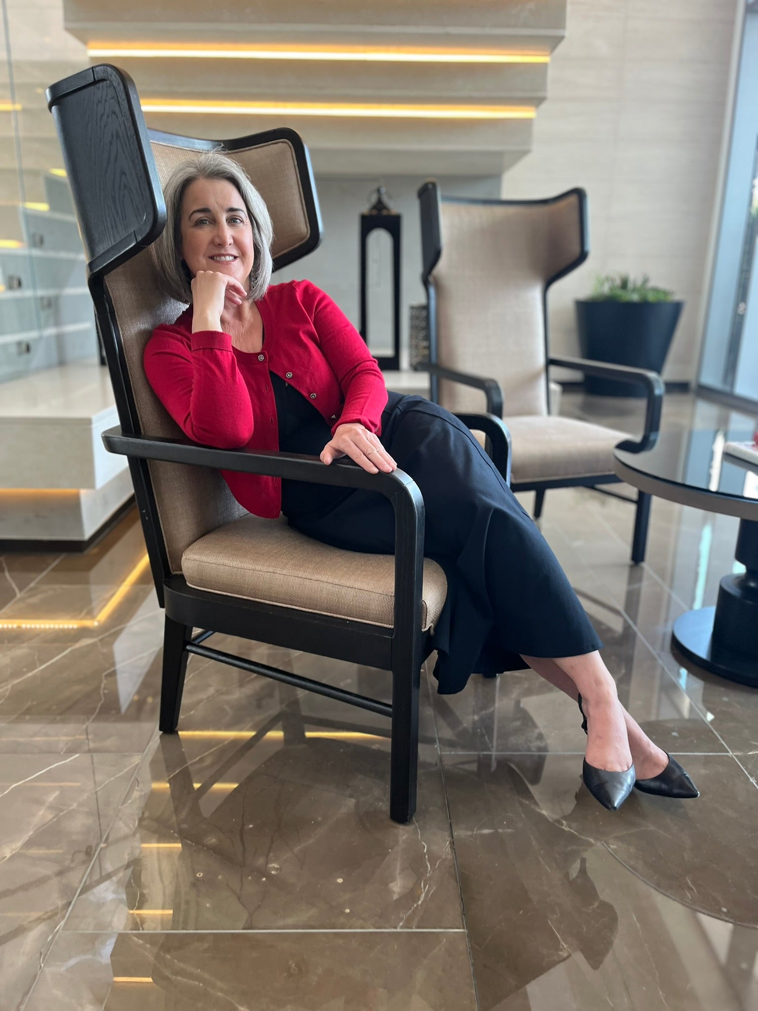 Woman relaxed in a chair,wearing long black dress with a red sweater.
