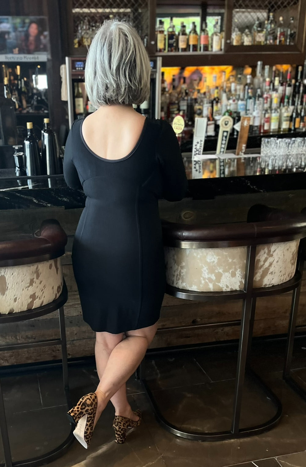 Back view of woman standing at bar, wearing black dress with scoop back.
