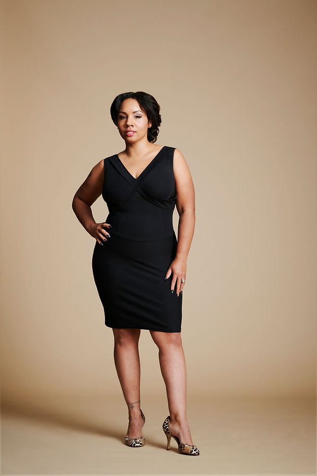 Women posed with right hand at waist, left leg slightly forward, wearing a black dress.