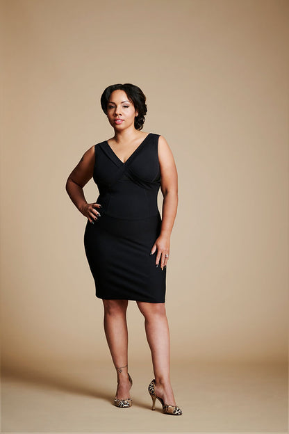 Women posed with right hand at waist, left leg slightly forward, wearing a black dress.