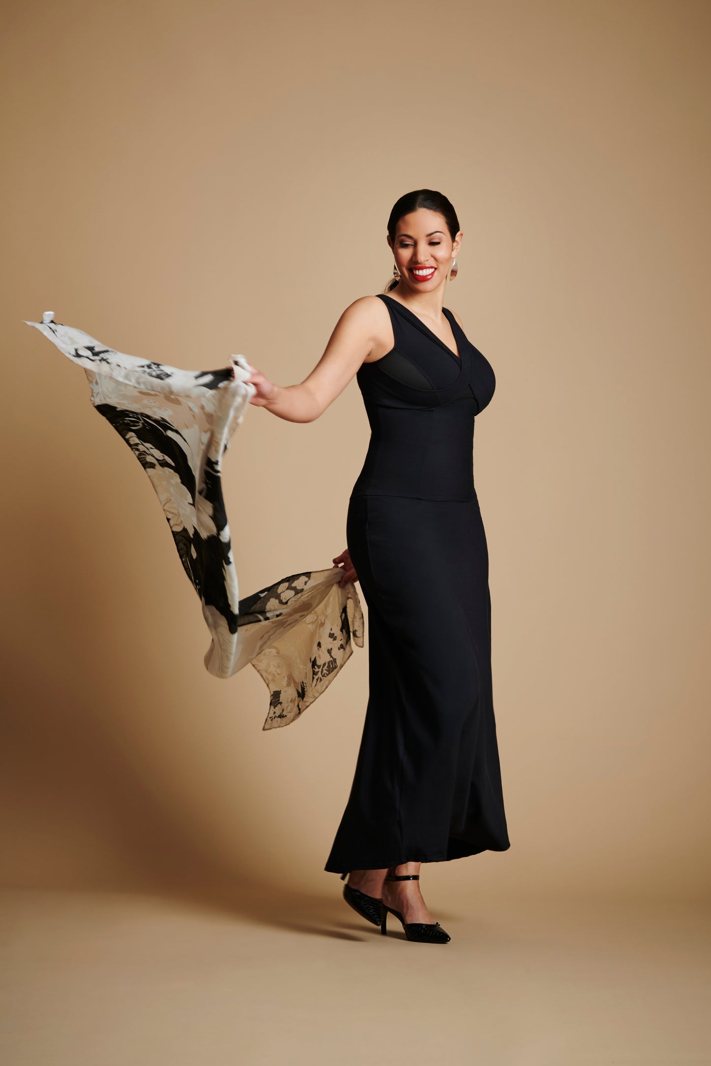 Woman wearing long black dress and holding scarf behind her with both hands.