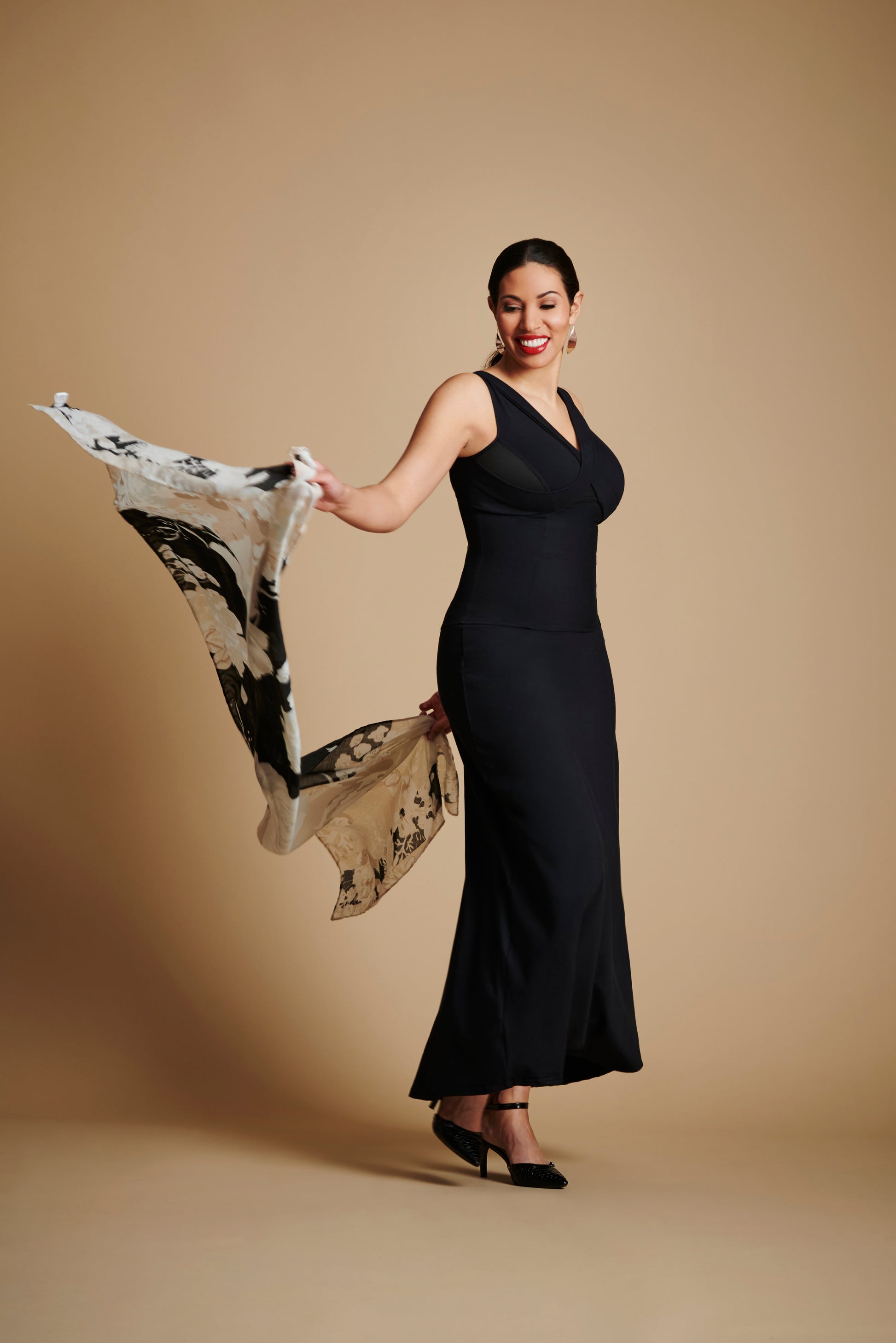 Woman wearing long black dress and holding scarf behind her with both hands.