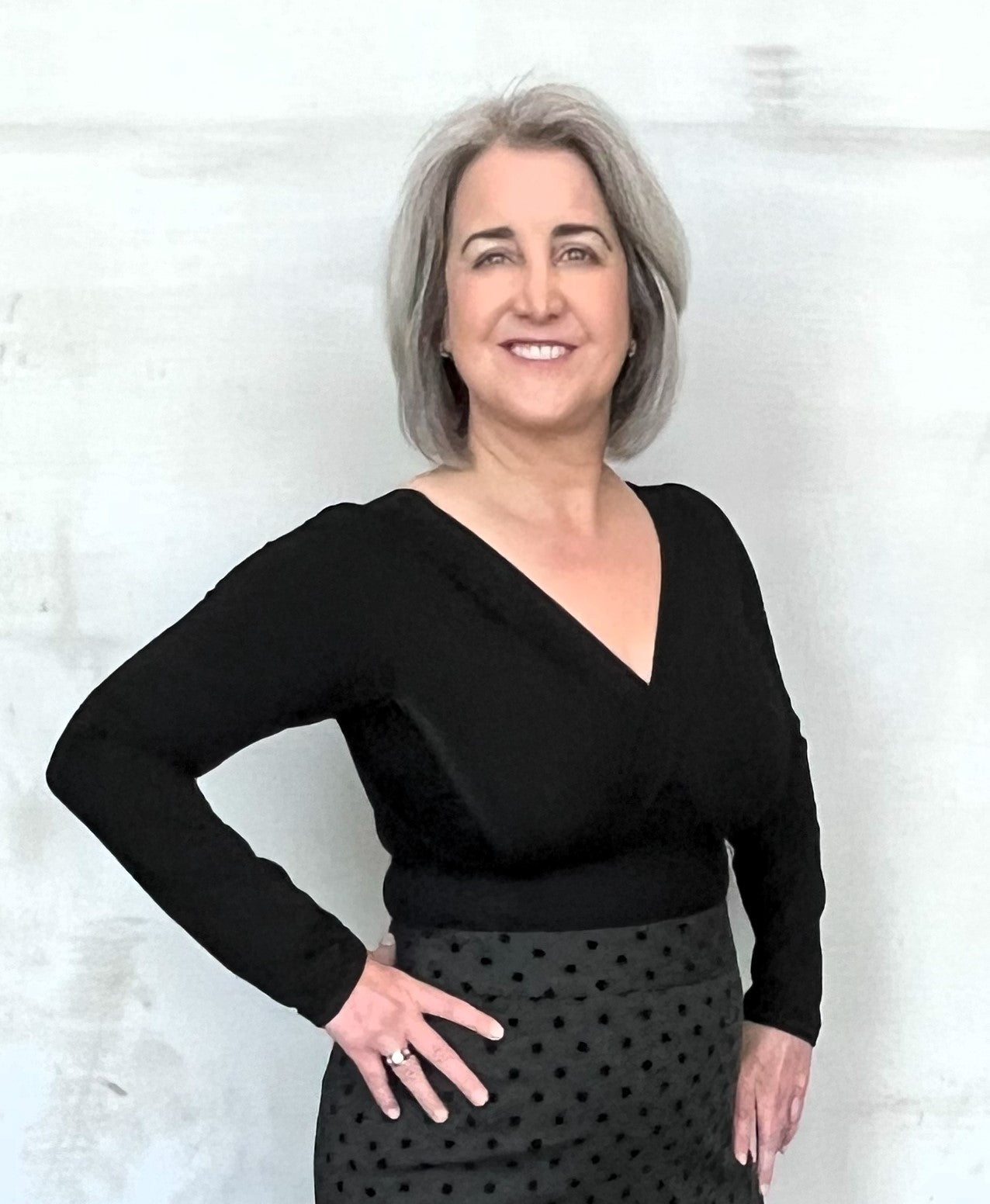 Woman wearing  black long sleeve v-neck top with right hand at waist.