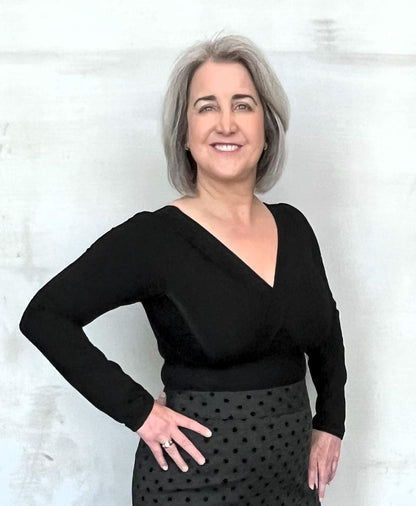 Woman wearing  black long sleeve v-neck top with right hand at waist.