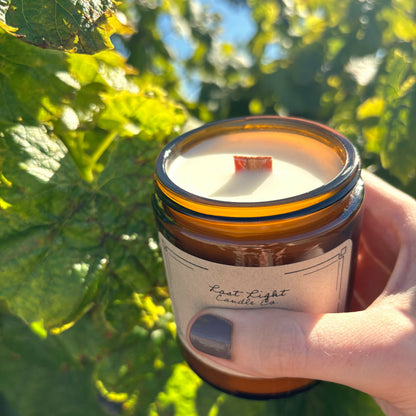 Hand holding out candle in amber jar with wood wick.