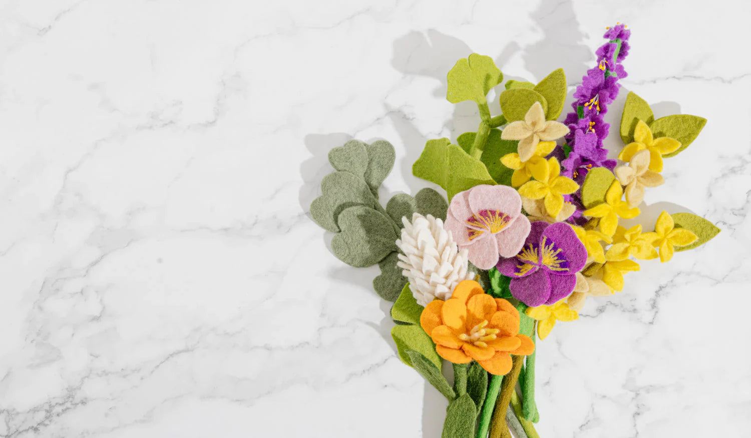 Yellow felt forsythia flower in a bunch of various felt flowers on a white marble counter.