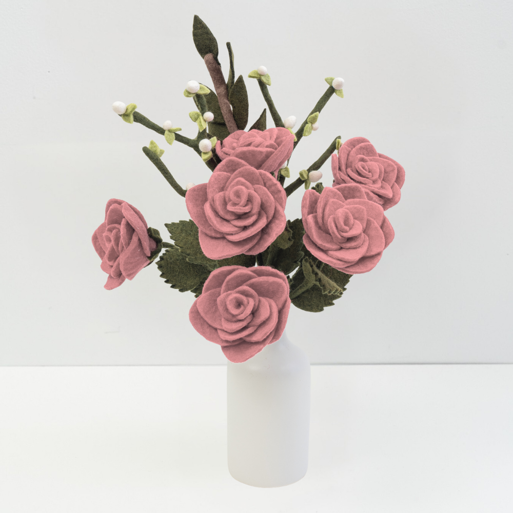 Felt flower bouquet of pink roses and white buds in a white vase with white background.