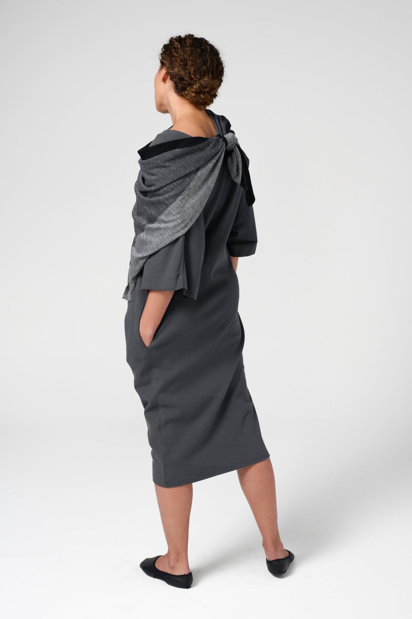 Back view of woman wearing black dress with black, charcoal, and grey modern Extrafine Merino wool scarf.