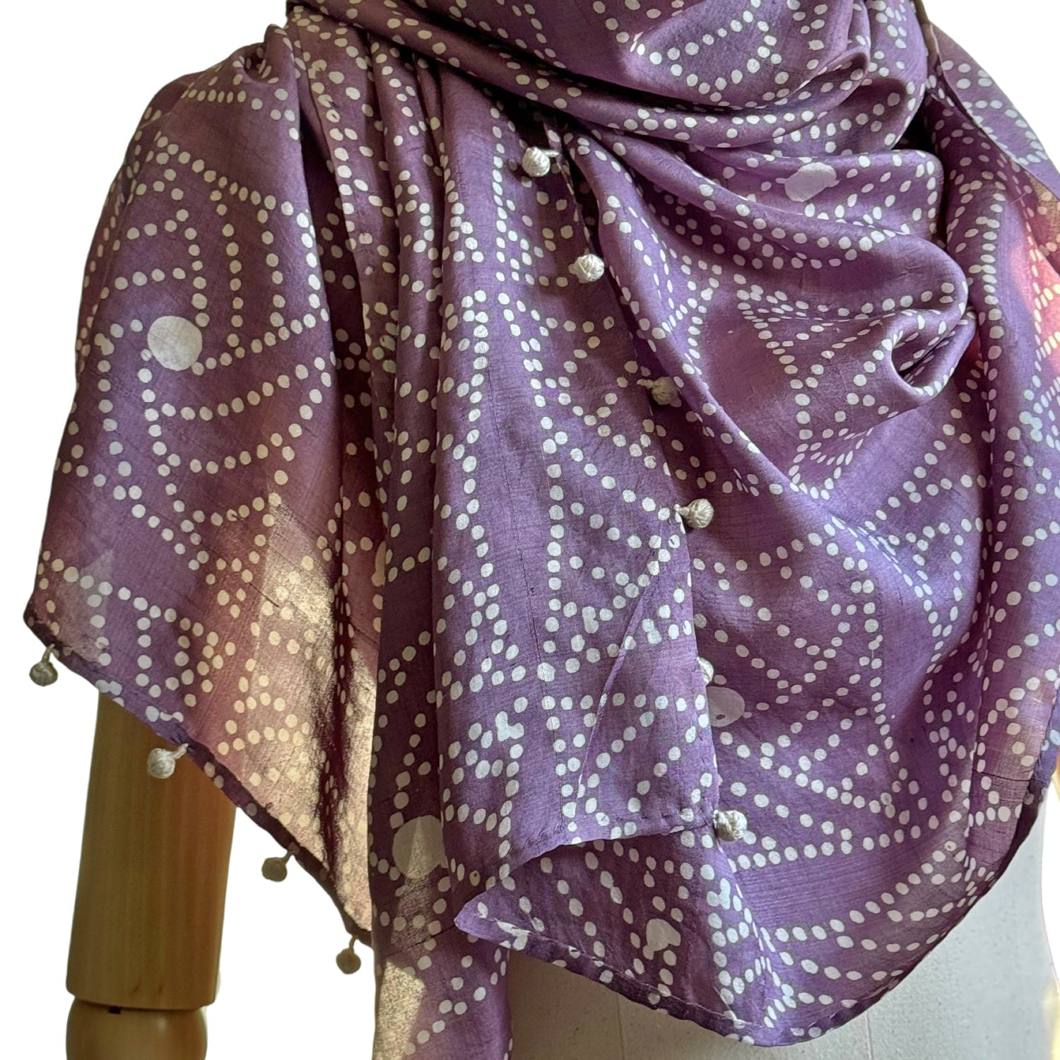 Closeup of purple and white batik scarf worn on wooden manikin. 