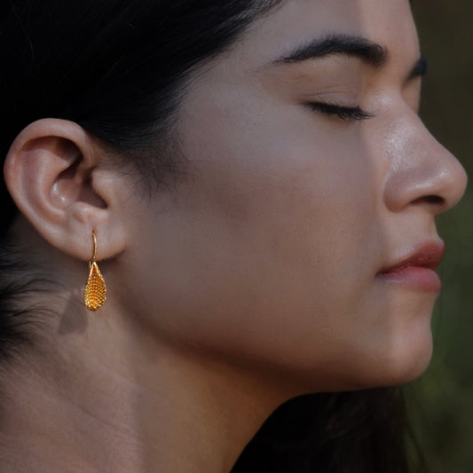 Front right view of woman wearing gold plated beeja Pod earrings.