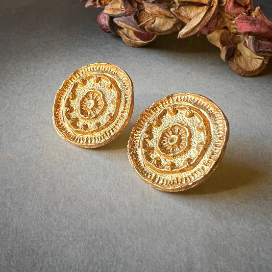 Pair of gold mandala earrings on grey background.