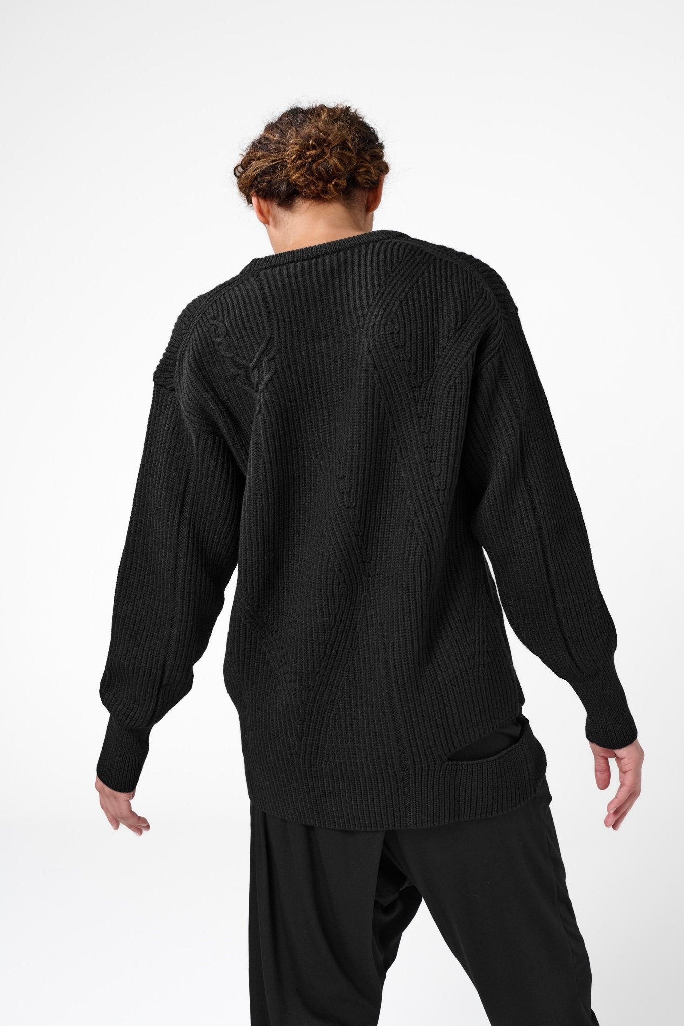 Back view of woman with arms slightly lifted from sides wearing black crewneck sweater with asymmetric ribbed design.