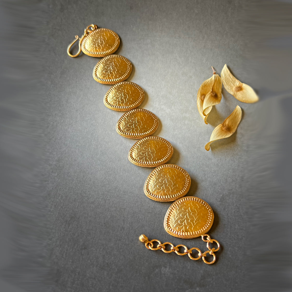 Gold bracelet with leaflet design in open vertical position on grey background.