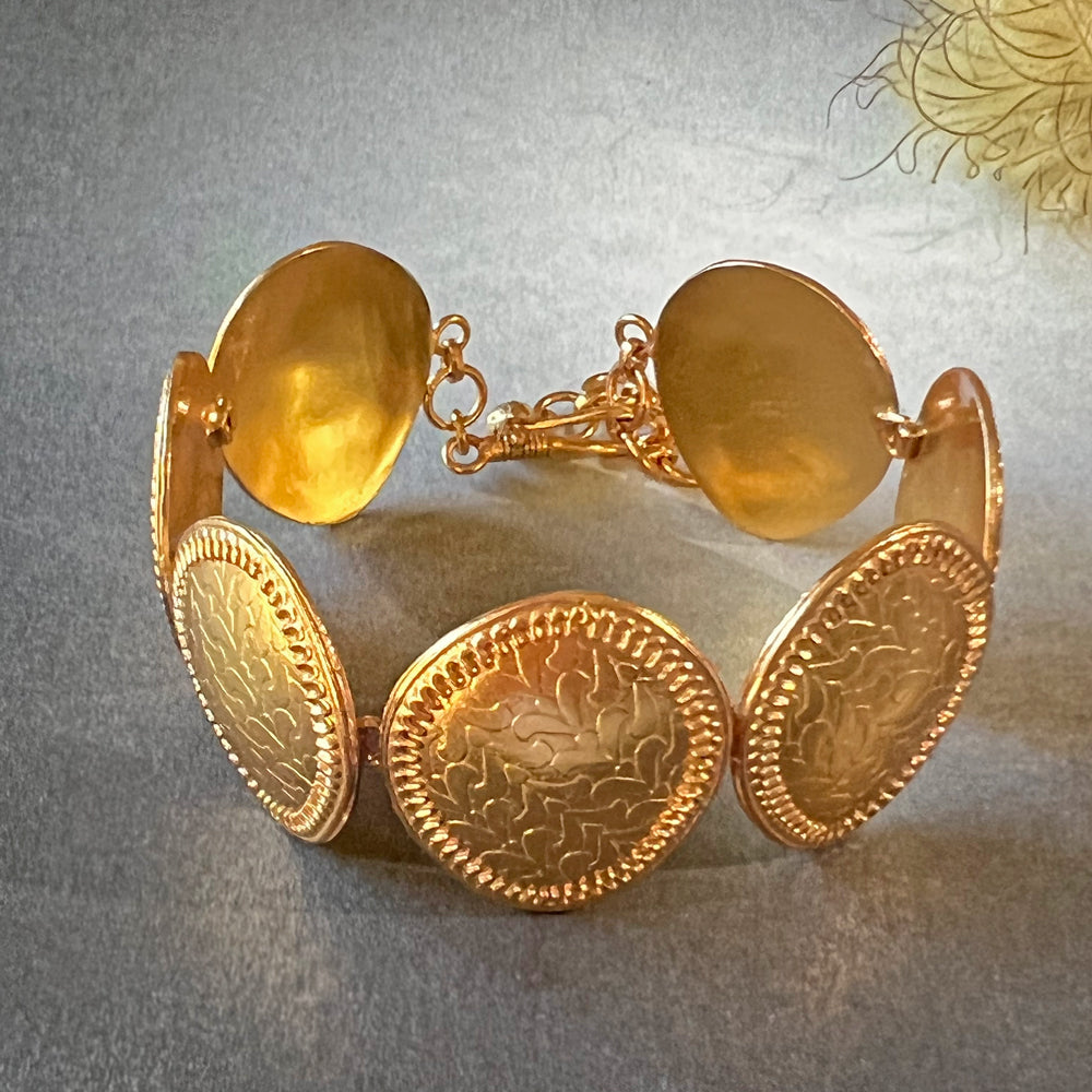 Gold bracelet with leaflet design on grey background.