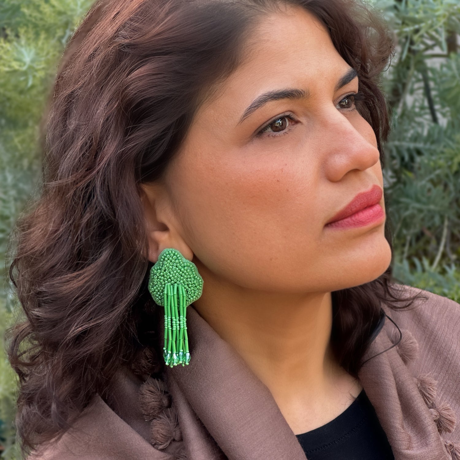 Front right view of woman wearing beaded green glass tassel earrings.