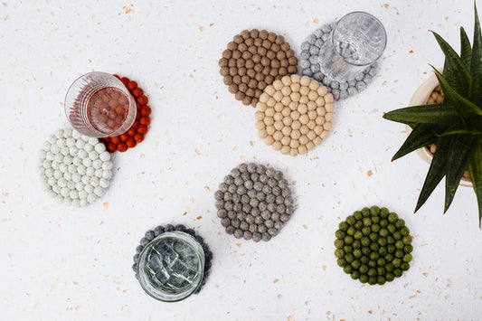 Felt circle coasters in red, green, brown, yellow, and various shades of grey scattered on a marble countertop.