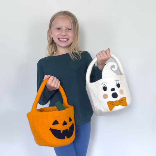 Blond girl holding orange felt jack-o-lantern trick-or-treat bucket and a white felt ghost trick-or-treat bucket with orange bow tie.