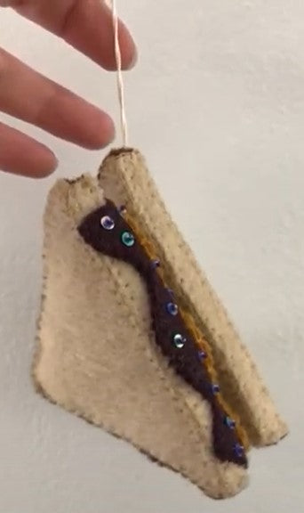 Close up of Felt ornament of a triangle cut PB&J being held by a hand.