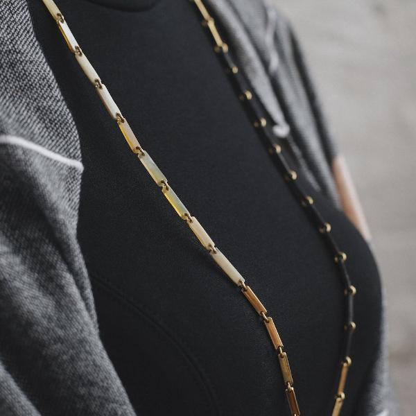 Close up of white, gold, and black link necklace on a woman in a black dress and grey shawl.
