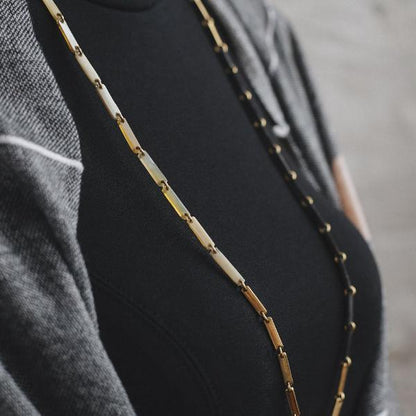 Close up of white, gold, and black link necklace on a woman in a black dress and grey shawl.