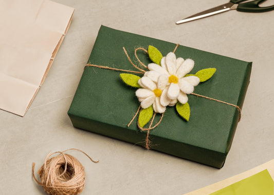 Two white daisies with green leaves and yellow centers felt gift topper shown around green wrapped gift.