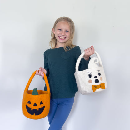 Blond girl holding orange felt jack-o-lantern trick-or-treat bucket and a white felt ghost trick-or-treat bucket with orange bow tie.