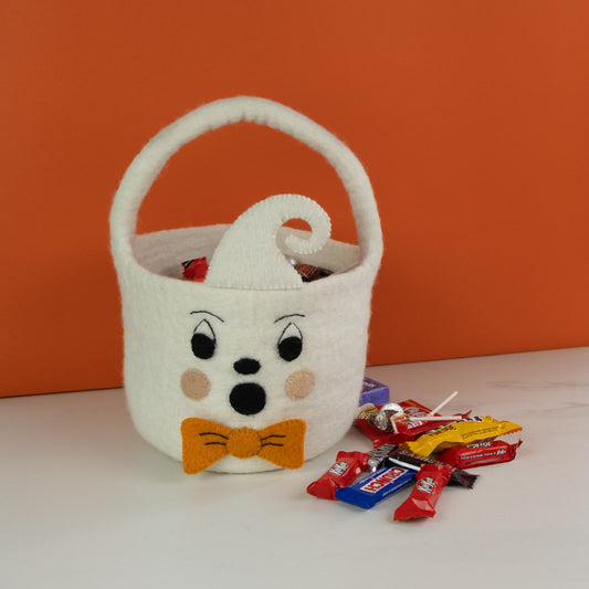 White felt ghost trick-or-treat bucket with orange bow tie and wrapped candy next to it.