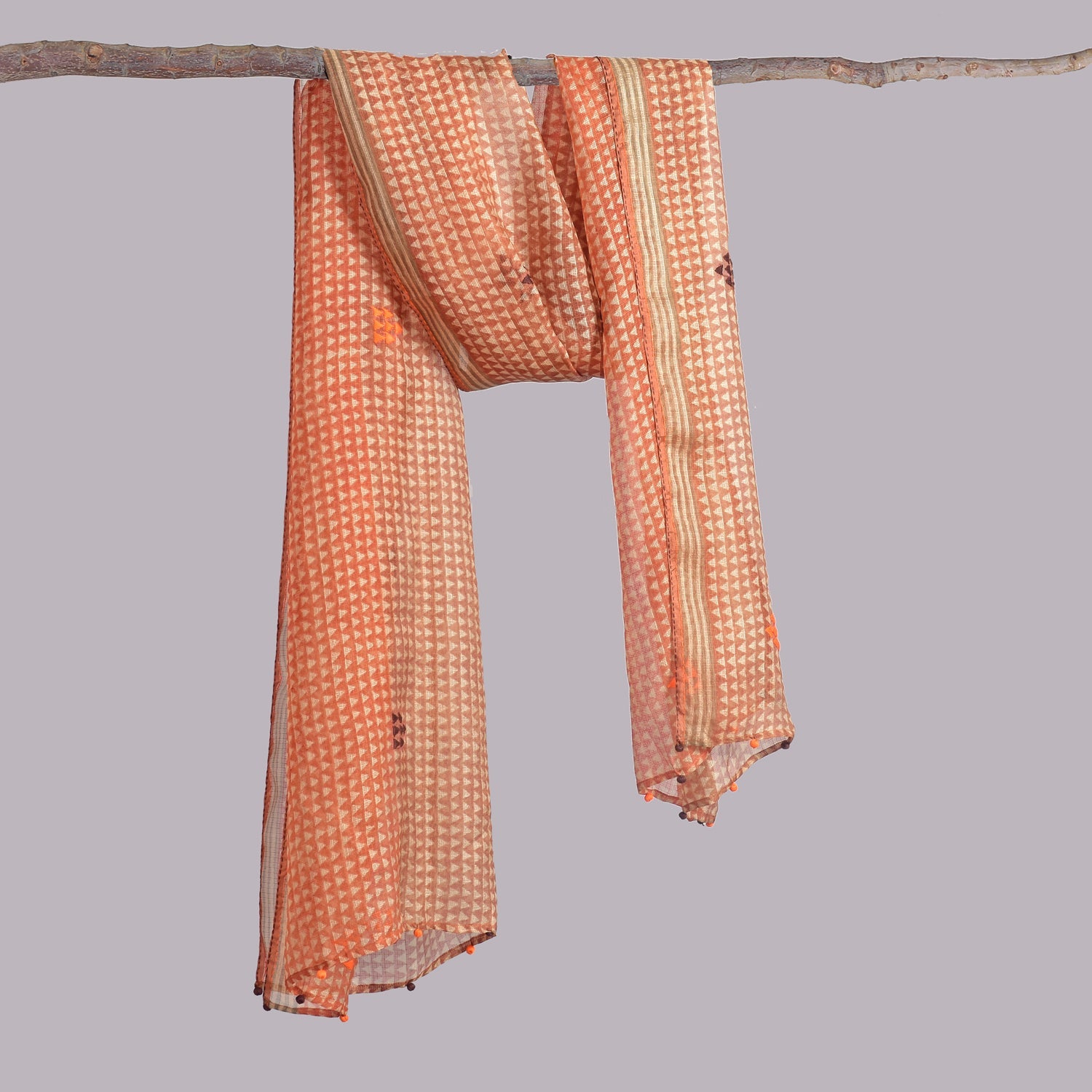 Orange and natural shoulder wrap draped over tree branch.