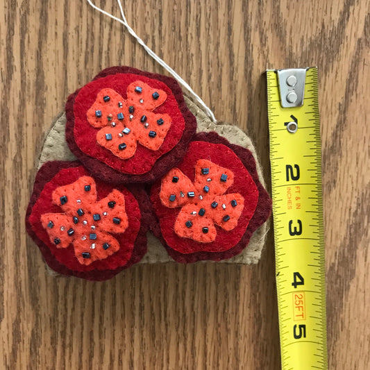 Felt ornament of three tomato slices on toast measuring about 3 inches wide.