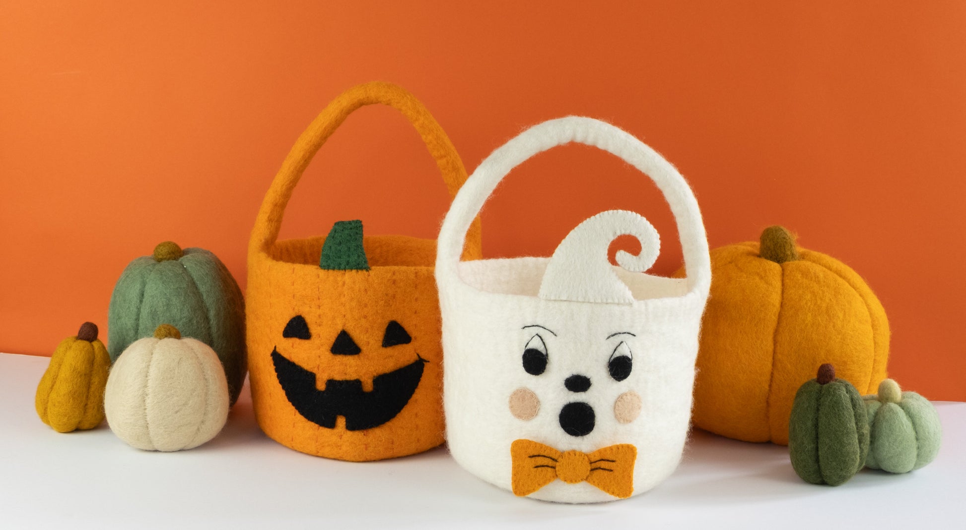 Orange felt jack-o-lantern trick-or-treat bucket and a white felt ghost trick-or-treat bucket with orange bow tie and felt pumpkins behind them.