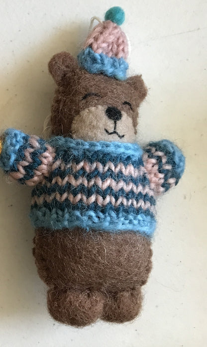 Close up of a felt ornament of a bear in a blue and pink striped knitted sweater and hat.